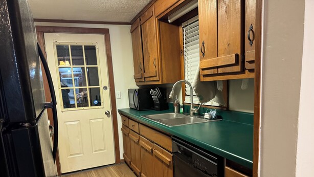 Una cocina con armarios de madera, lavavajillas, fregadero y una puerta que da a un garaje.