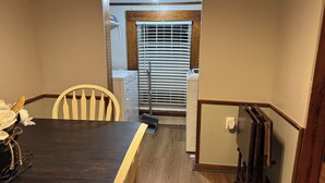 Un comedor con una mesa de madera oscura, una silla blanca y una escoba apoyada en la pared.