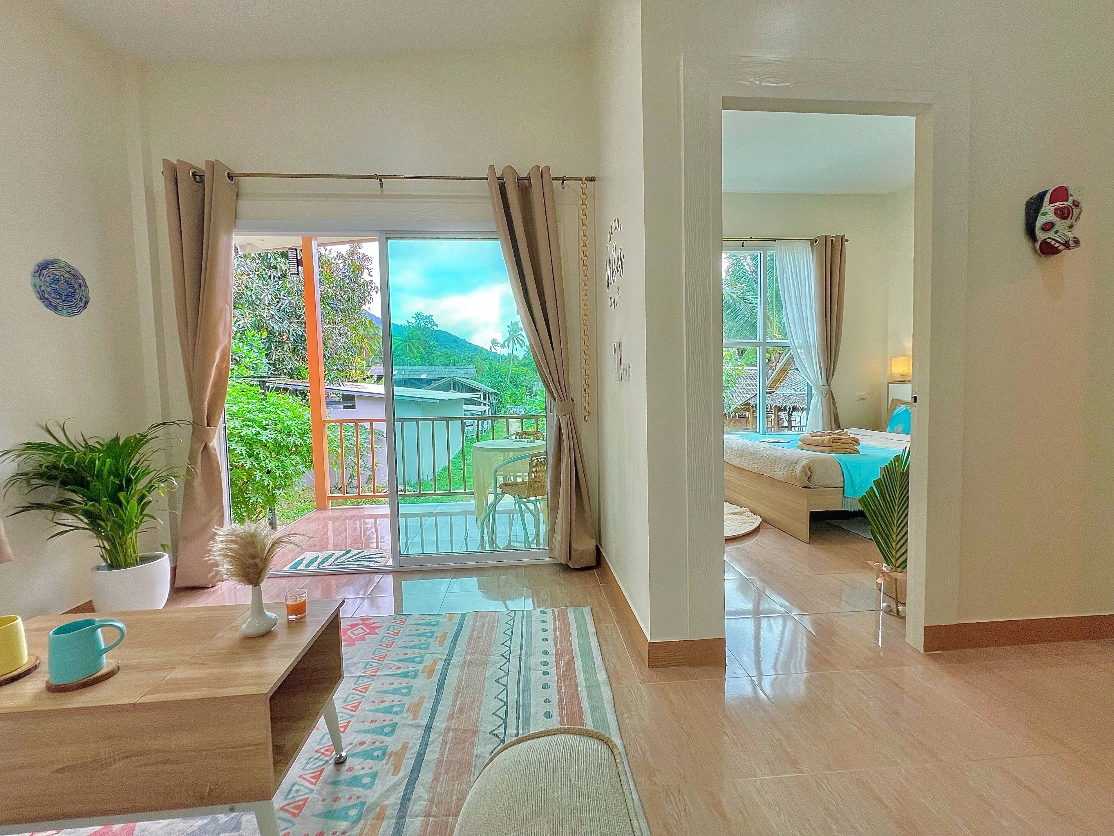 Una habitación con balcón, cama, escritorio y una planta en maceta.