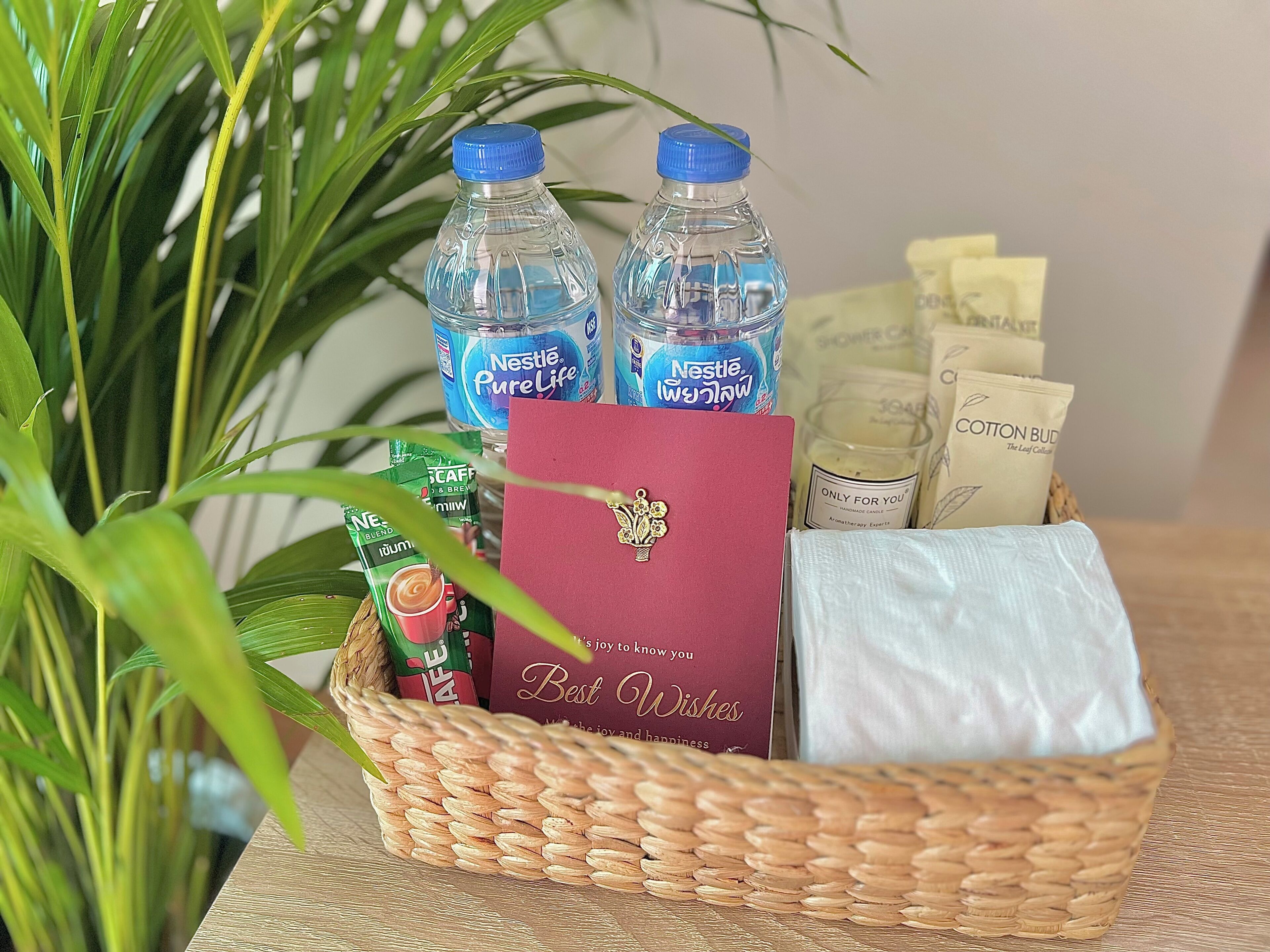 A wicker basket containing a red card, two Nestle PureLife water bottles, a green sachet, and a white cloth.