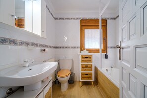 Kylpyhuone, jossa on valkoinen pesuallas, wc-istuin ja puinen kaappi.