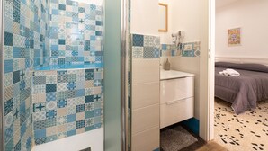 Une salle de bain avec des carreaux décorés, une douche, un lavabo avec un miroir et un lit avec une couverture.
