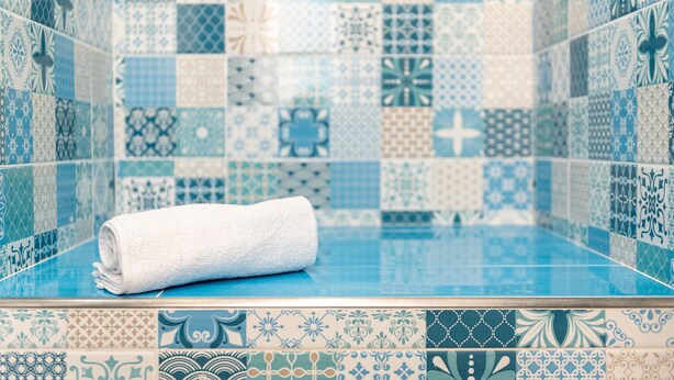 Une salle de bain avec un mur recouvert de carreaux bleus et une serviette blanche enroulée sur le sol.