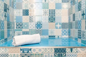A bathroom with a blue tiled wall and a rolled white towel on the floor. - Holiday House Annunziata 2 Apartment with Balcony, Wi-Fi and Air Conditioning (Termini Imerese)