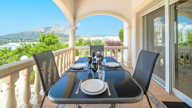A dining table set on a balcony with a mountain view, white balustrades, and a glass door. - Holiday Home 'Del Sol' with Mountain View, Wi-Fi, and Air Conditioning (Xàbia)