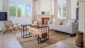 A living room with a sofa, a wooden bench, a small table, a TV, and a fireplace. - Holiday Home 'Del Sol' with Mountain View, Wi-Fi, and Air Conditioning (Xàbia)