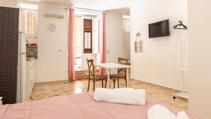A bedroom with a bed, a desk, and a chair, a television, and a bathroom visible through an open door. - Holiday House Annunziata 1 Apartment with Wi-Fi and Air Conditioning (Termini Imerese)