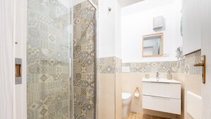 A bathroom with patterned tiles, a glass shower enclosure, a toilet, and a white sink with a mirror above it. - Holiday House Annunziata 1 Apartment with Wi-Fi and Air Conditioning (Termini Imerese)