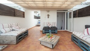 A covered outdoor seating area with two sofas, a coffee table with fruits, and a rustic wall.