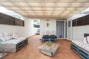 A covered outdoor seating area with two sofas, a coffee table with fruits, and a rustic wall.