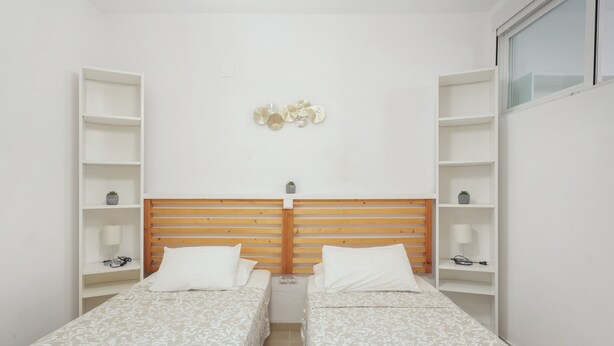 A small, clean room with two single beds, a wooden headboard, and white walls.