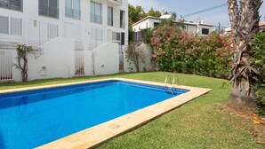 A swimming pool with a clear blue water surface, surrounded by a well-maintained lawn and a white building with multiple windows and balconies.