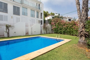 A swimming pool with a clear blue water surface, surrounded by a well-maintained lawn and a white building with multiple windows and balconies.