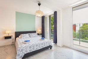 A modern bedroom with a large bed, two bedside lamps, a ceiling light, and a view of the outdoors through a sliding glass door. - Vacation Home 'Adosado A Un Paso Del Mar' with Shared Pool, Wi-Fi and Air Conditioning (Xàbia)