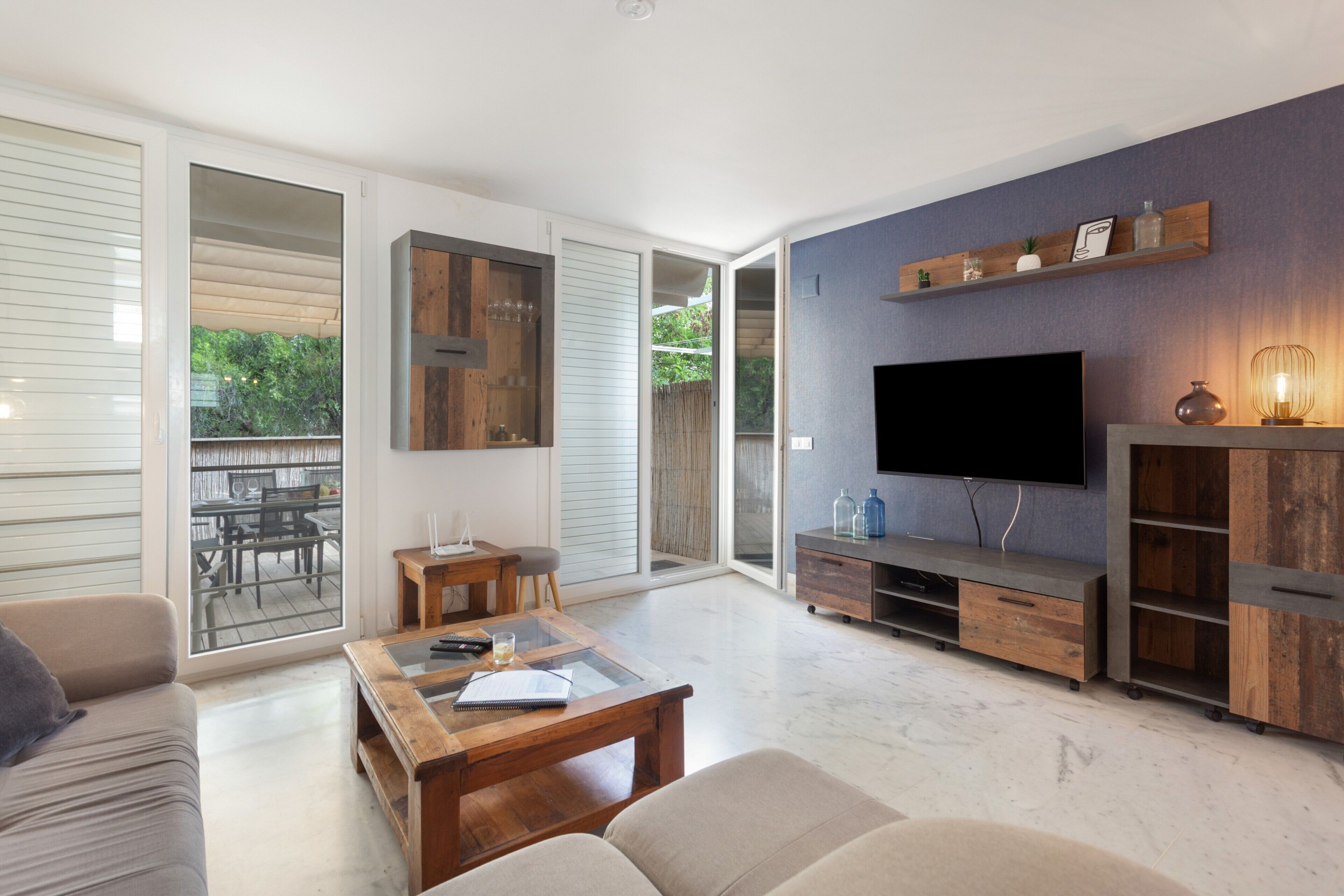A modern living room with a flat-screen TV, wooden furniture, and a sliding glass door leading to an outdoor area.