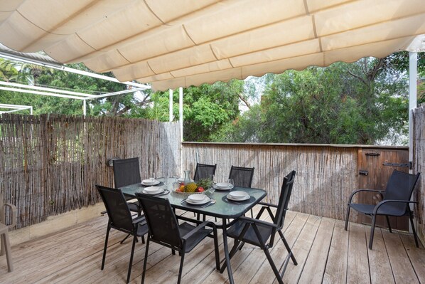 Une terrasse extérieure avec une table dressée pour le repas, entourée de chaises, et une clôture en bambou.