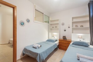 A bedroom with two single beds, a wooden dresser, a mirror, and wall-mounted shelves with decorative items. - Vacation Home 'Adosado A Un Paso Del Mar' with Shared Pool, Wi-Fi and Air Conditioning (Xàbia)