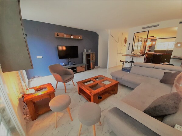 Ein modernes Wohnzimmer mit einer Couch, Sesseln, einem Couchtisch und einem Fernseher.