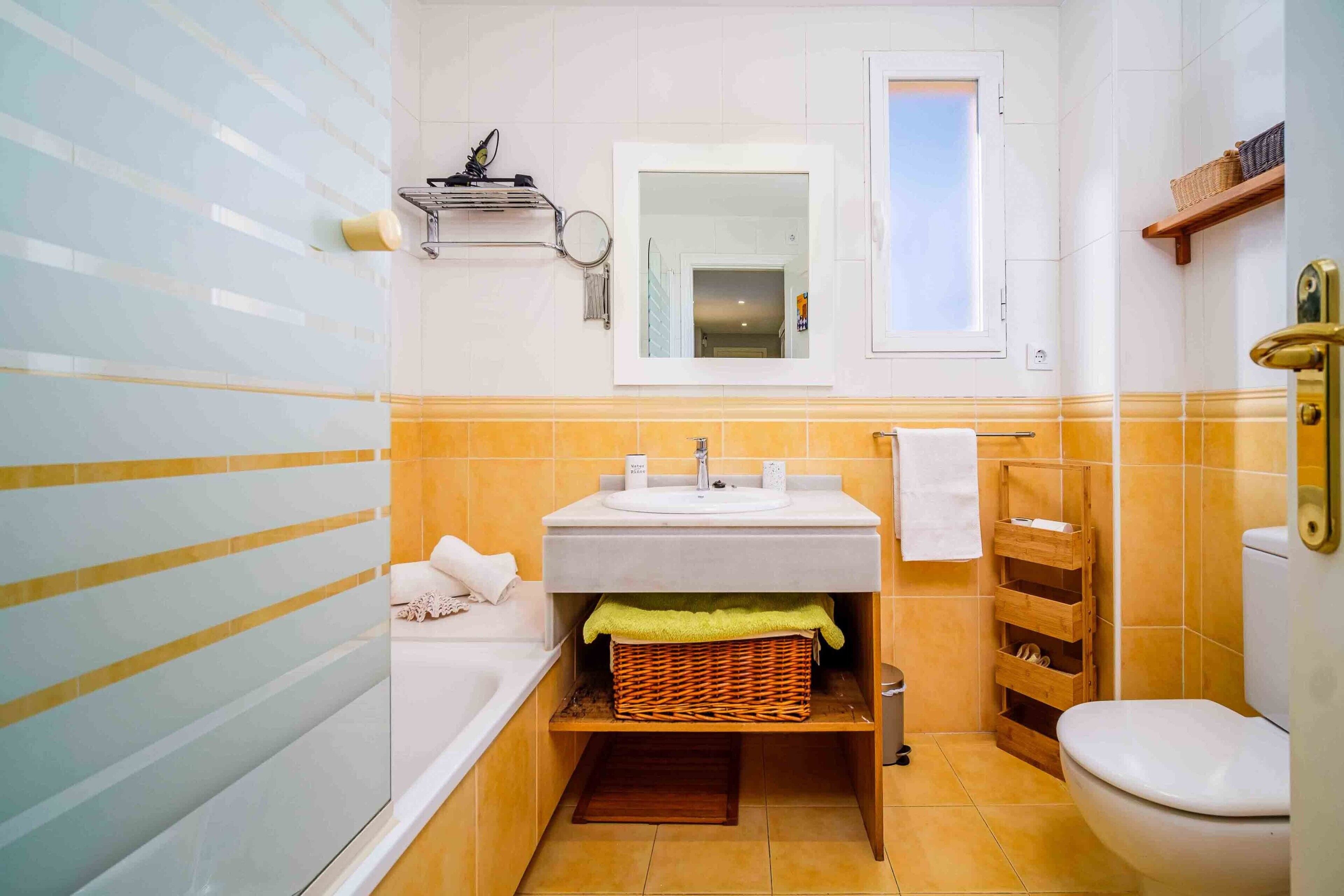 Een badkamer met bad, wastafel en toilet, met een spiegel, handdoekhouder en opbergplanken.