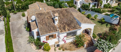 Una casa residencial con techo de tejas, una antena parabólica y un pequeño jardín con plantas en flor.