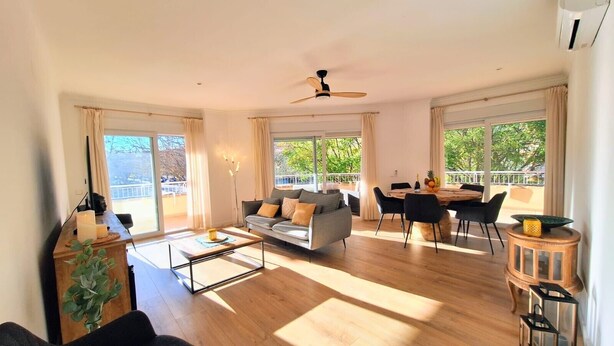 Un vaste espace de vie comprenant un canapé, une table à manger et des chaises, de grandes fenêtres et un ventilateur de plafond.