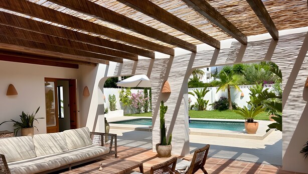 Un patio iluminado por el sol con un sofá, sillas y una mesa, con vistas a una piscina y un jardín exuberante.