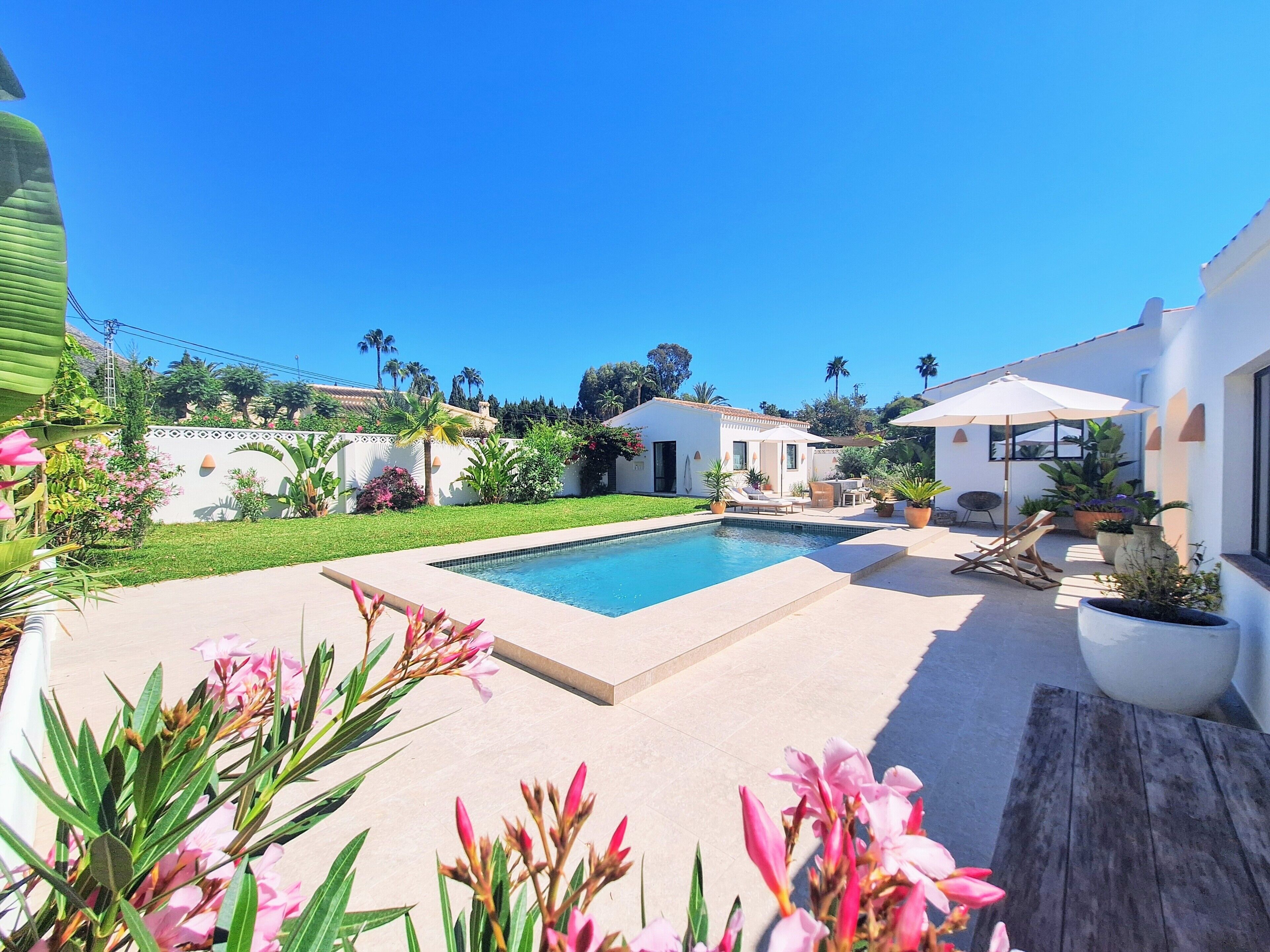 A pool area with a clear blue sky, a white building, and potted plants.
