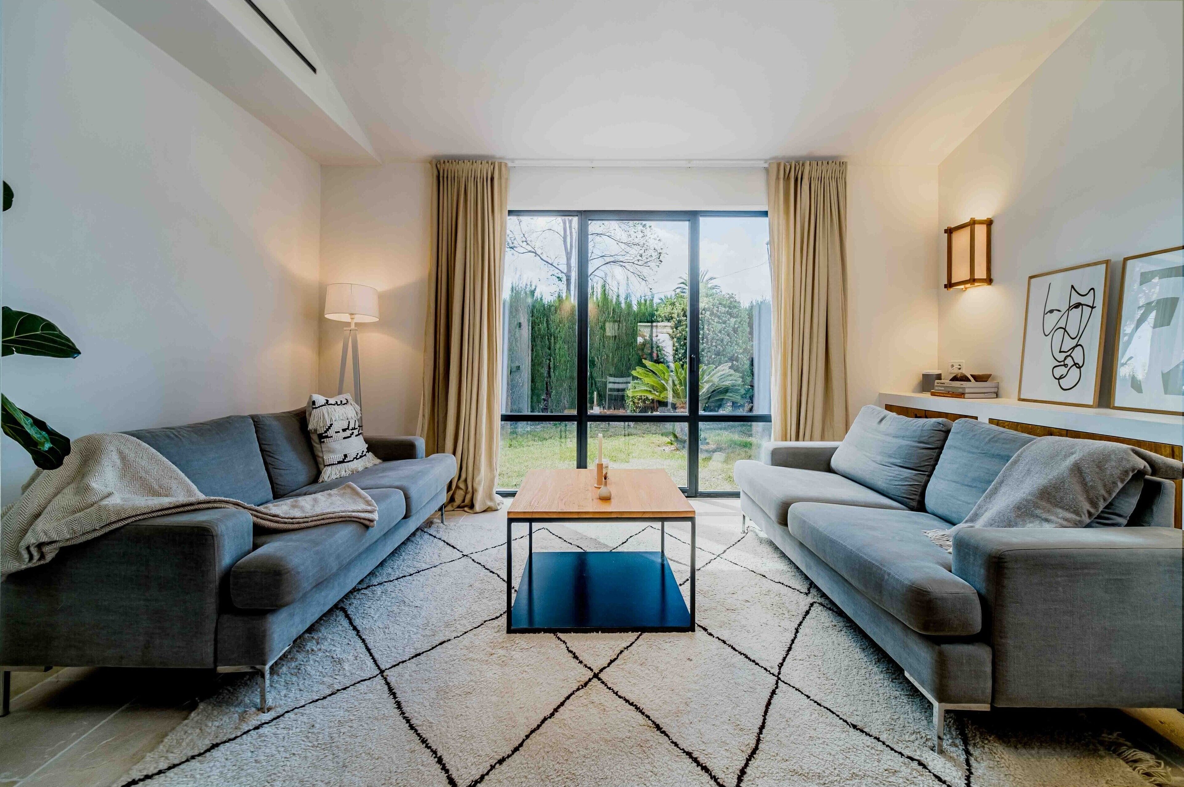 Un salon moderne avec deux canapés, une table basse et une grande fenêtre agrémentée de rideaux.