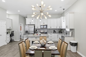 A modern kitchen with white cabinets, a central island, and a chandelier. - Hot Tub~Spa Shower~BBQ~Fire Pit~Near DT (Indianapolis)