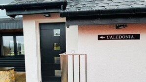 Een gevel met een zwarte deur, een metalen hek en een bord waarop 'CALEDONIA' staat.