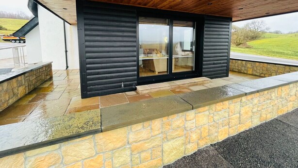 Een modern gebouw met een stenen fundering, een houten plafond en een grote schuifglazen deur.