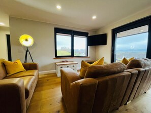 Un salon avec des canapés en cuir, une lampe sur pied, un téléviseur et une fenêtre donnant sur un beau paysage.