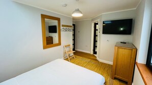 Een slaapkamer met een bed, een houten stoel, een televisie, een kledingkast en een spiegel.