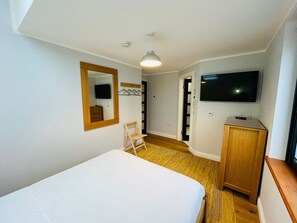 Une chambre à coucher avec un lit, une chaise en bois, une télévision, une armoire et un miroir.