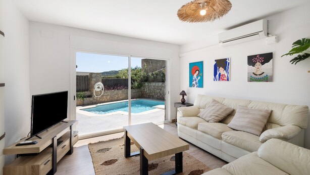 A living room with a TV, sofa, coffee table, and a view of a swimming pool. - Ground Floor Apartment with Private Pool (Sa Riera)