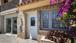 A stone building with a white door, a window with metal bars, and a garden with purple flowers. - Ground Floor Apartment with Private Pool (Sa Riera)