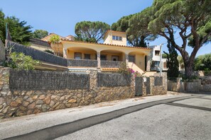 Un edificio de dos pisos con un muro de piedra, un balcón y un árbol grande.