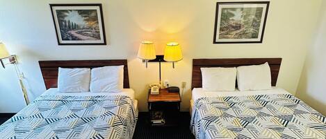 Habitación de hotel con dos camas, una mesita de noche, una lámpara y dos cuadros en la pared.