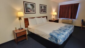 Una habitación de hotel con una cama, dos lámparas de noche, una mesita de noche, un aire acondicionado instalado en la pared y dos cuadros enmarcados.