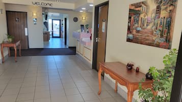 A hotel reception area with a reception desk, a 'Welcome' sign, a clock, and a painting on the wall.