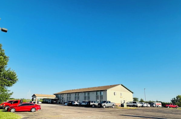 A parking lot with multiple vehicles, a building with a flat roof, and a clear blue sky.