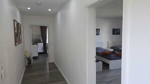 Un pasillo que da a un dormitorio con cama, una pequeña kitchenette y una puerta.