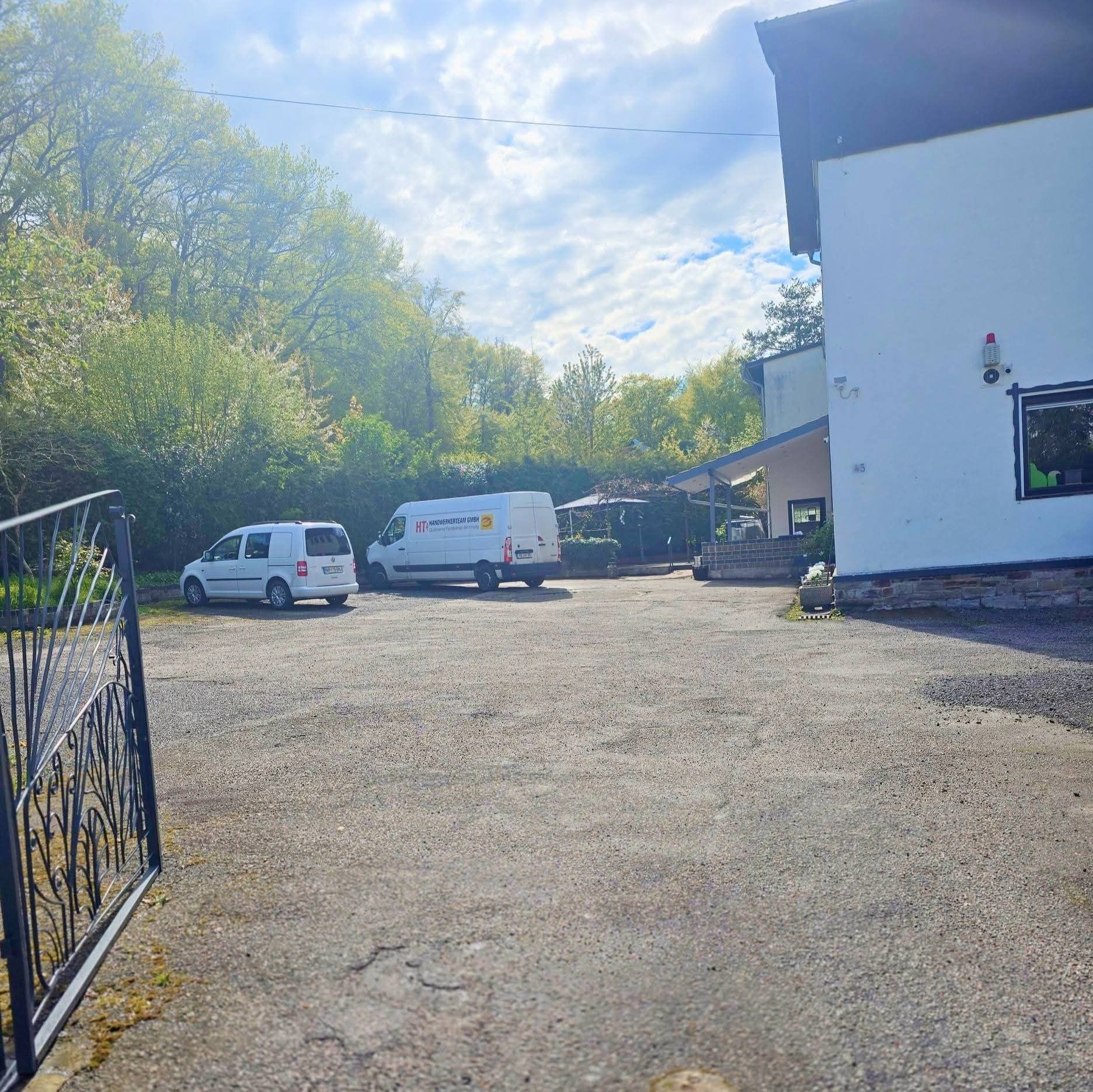 A gravel parking area with two white vans parked in front of a building with a white exterior and a small window with a green object inside.