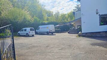 A gravel parking area with two white vans parked in front of a building with a white exterior and a small window with a green object inside.