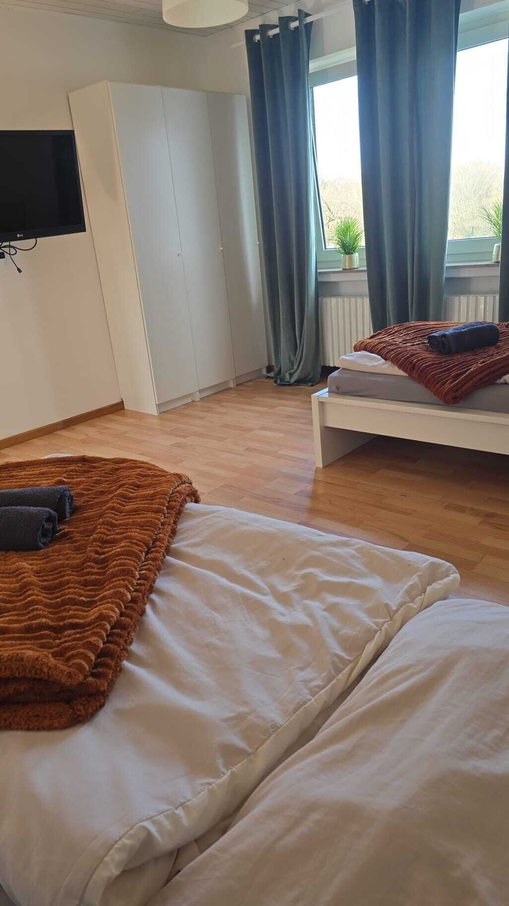 Une chambre à coucher avec un lit, un téléviseur fixé au mur, une fenêtre avec des rideaux et un radiateur.