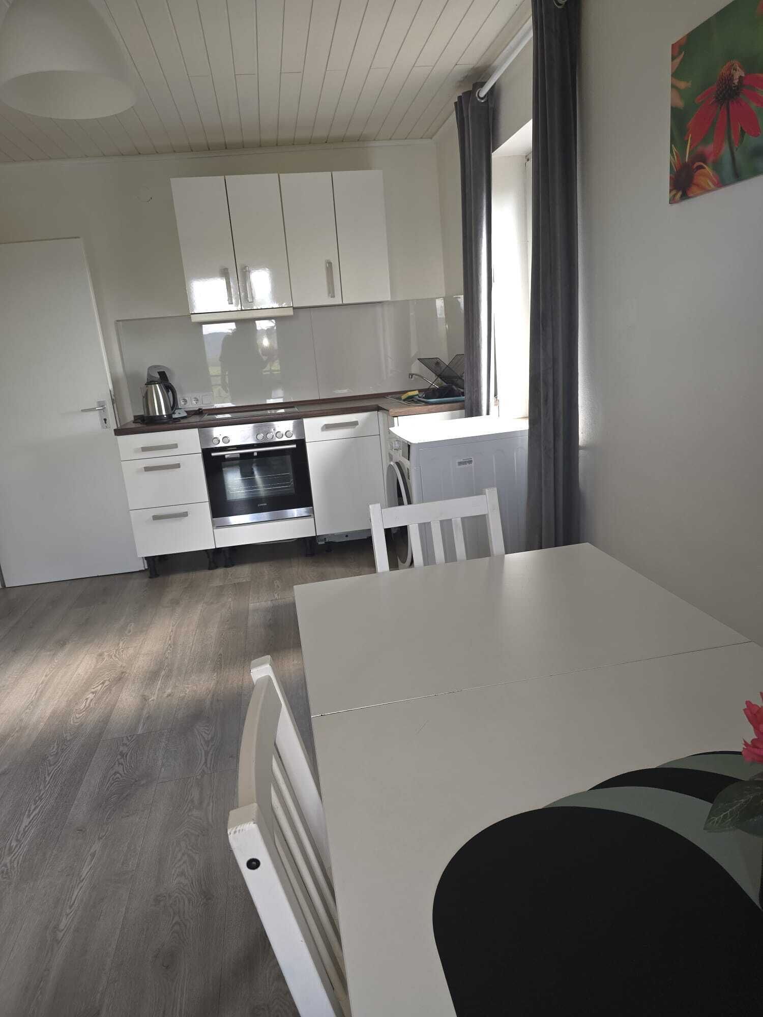 A modern kitchen with white cabinets, a built-in oven, and a dining area with a table and chairs.