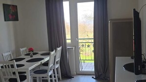 Una habitación con una mesa de comedor, sillas, un televisor y una ventana con cortinas.