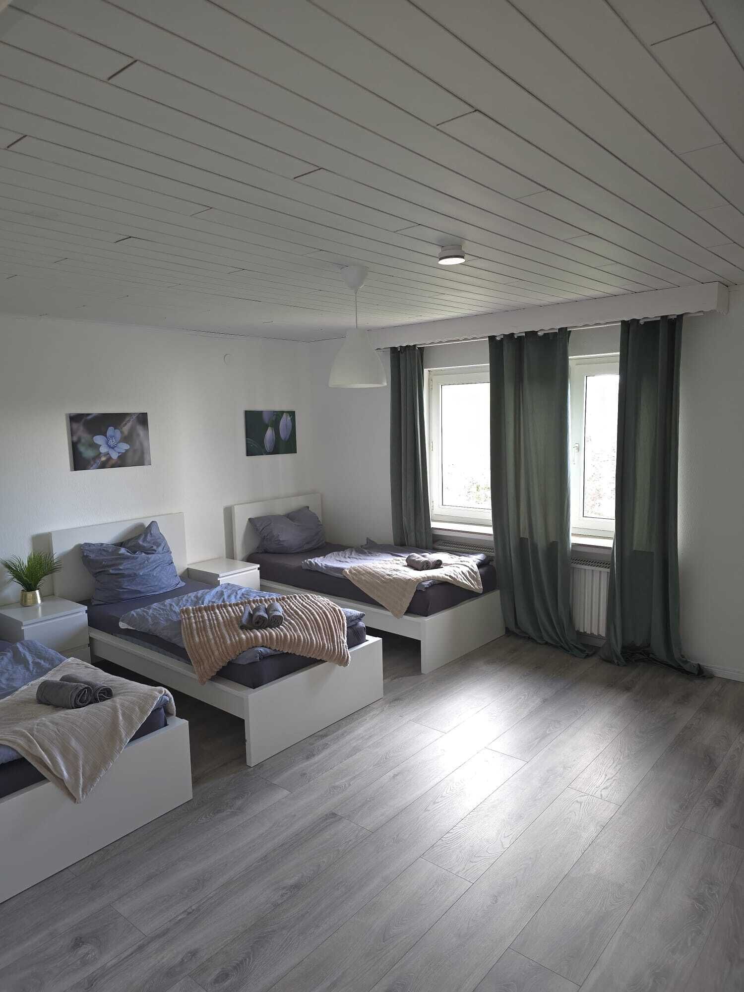 A modern bedroom with three beds, a white ceiling, and a large window with curtains.