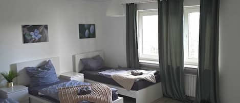 A modern bedroom with three beds, a white ceiling, and a large window with curtains.