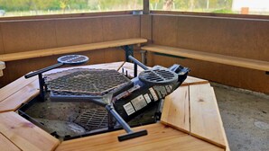 Una mesa de parrilla hexagonal de madera con parrilla de carbón integrada, rodeada de bancos de madera.